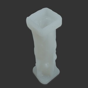 May include: White plastic mold for making candles. The mold is shaped like a square column with a round opening at the top.