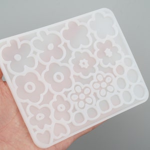 Peut inclure: Moule en silicone blanc avec plusieurs formes de fleurs et de cercles. Le moule est flexible et peut être utilisé pour réaliser des objets en résine.