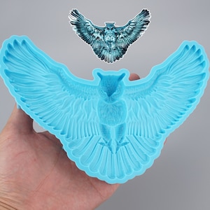 Pode incluir: Uma forma de silicone azul em forma de coruja com as asas abertas. A forma é projetada para criar um bolo ou outro item comestível em forma de coruja.