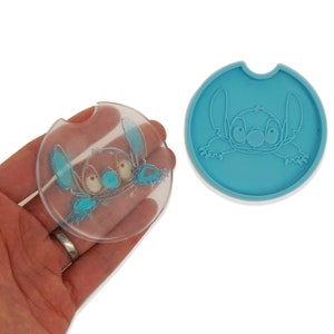 May include: Two car coasters featuring the character Stitch from the animated film Lilo & Stitch. One coaster is a clear, circular design with a blue Stitch outline. The other is a solid, light blue coaster with a raised Stitch design.