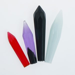May include: Four glass crystal points in different colors: red, purple, black, and white. The points are all sharp and have a faceted design.