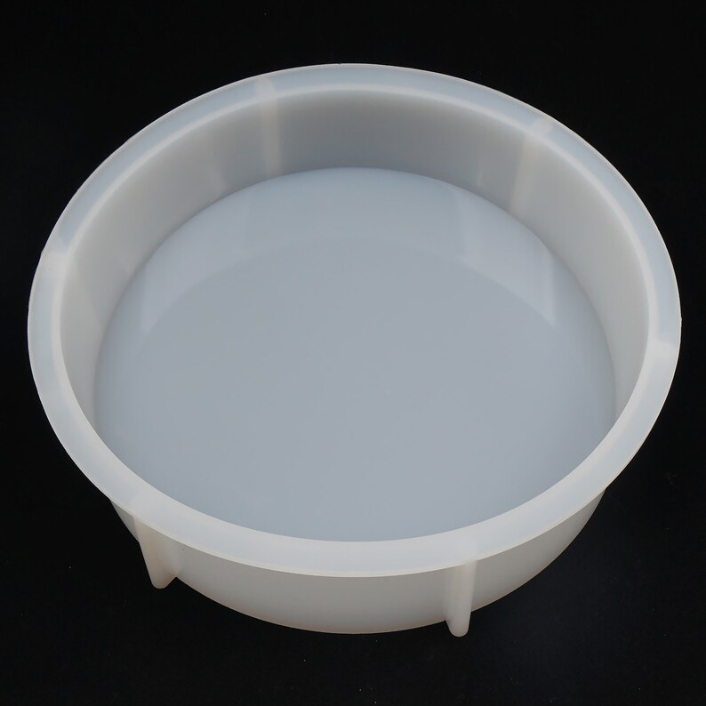 May include: A clear, round silicone mold with a shallow, bowl-like shape. The mold has a smooth, glossy interior and a slightly textured exterior. The sides are straight and the base is curved. The mold is designed for crafting and casting projects.