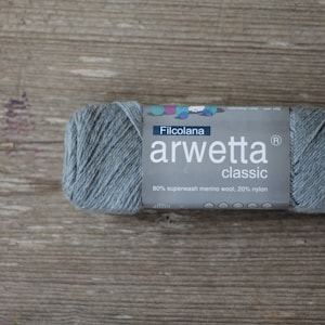 以下が含まれることがあります： 「Filcolana arwetta classic 80% superwash メリノウール、20% ナイロン」とラベル付けされた、薄い青色の糸の玉。