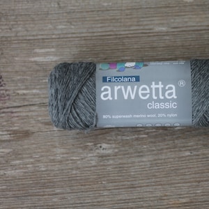Puede incluir: Un ovillo de lana gris con la etiqueta "Filcolana arwetta classic 80% lana merino superwash; 20% nylon".