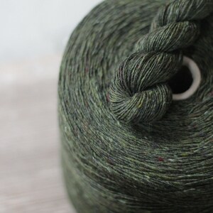 May include: A skein of dark green yarn with flecks of color. The yarn is wound around a white cardboard center.