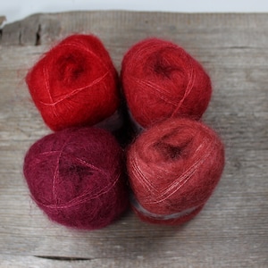 Pode incluir: Quatro novelos de lã em tons de vermelho, bordô e ferrugem. A lã é macia e fofa, e é perfeita para tricotar ou fazer crochê.