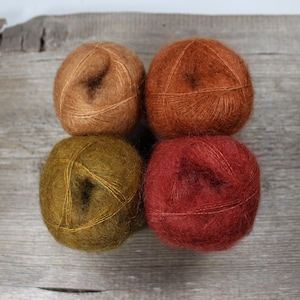 May include: Four balls of yarn in different shades of brown, orange, and red. The yarn is soft and fluffy, and it would be perfect for knitting or crocheting.