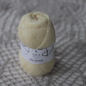 May include: A ball of pale yellow yarn with a white label that reads "SAGA 100% Icelandic Wool 50g/1.75oz Filcolana"