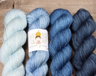 May include: Four skeins of yarn in shades of blue, from light to dark. The yarn is arranged in a row, with the label "maru.ma yarns" visible in the center.