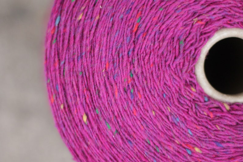 Puede incluir: Primer plano de un carrete de hilo rosa con motas multicolores. El hilo est&aacute; enrollado firmemente alrededor de un n&uacute;cleo de cart&oacute;n.