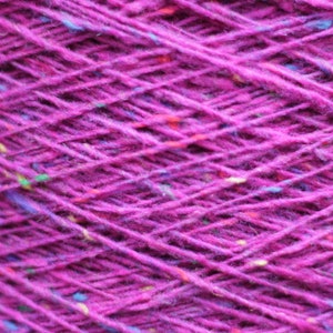 Puede incluir: Primer plano de un ovillo de hilo de color morado oscuro con motas de fibras multicolores tejidas en todo el ovillo.