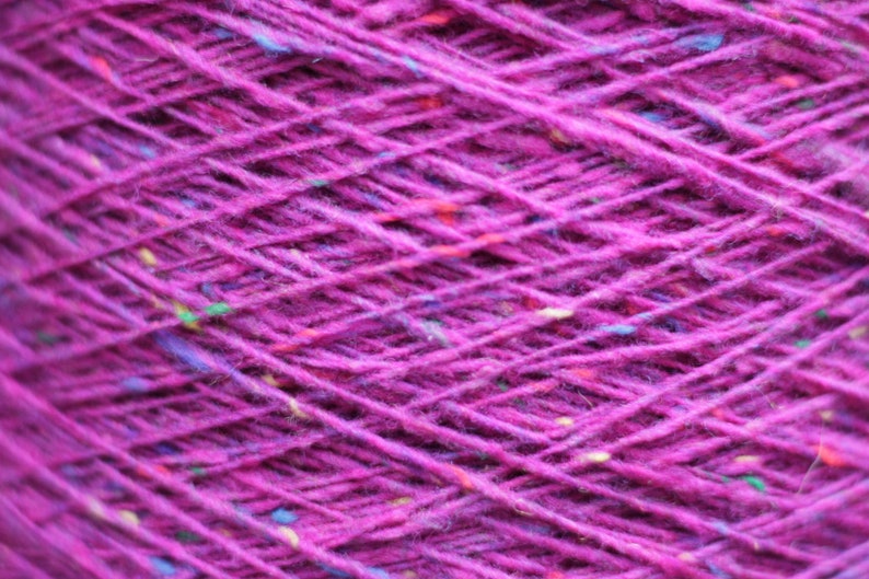 Puede incluir: Primer plano de un ovillo de hilo de color morado oscuro con motas de fibras multicolores tejidas en todo el ovillo.