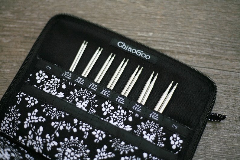 May include: A black zippered case with a white floral pattern lining. The case contains a set of eight ChiaoGoo knitting needles, labeled with US sizes 2 through 8.
