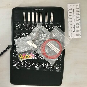 May include: A black zippered case with a white and black floral pattern holds a set of ChiaoGoo knitting needles. The needles are organized by size and include a variety of sizes. The case also includes a ruler, a set of stitch markers, and a set of cables.