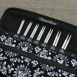 May include: A black zippered case with a white floral pattern holds a set of eight pairs of ChiaoGoo interchangeable knitting needles. The needles are labeled with US sizes 2 through 8, with corresponding millimeter measurements.