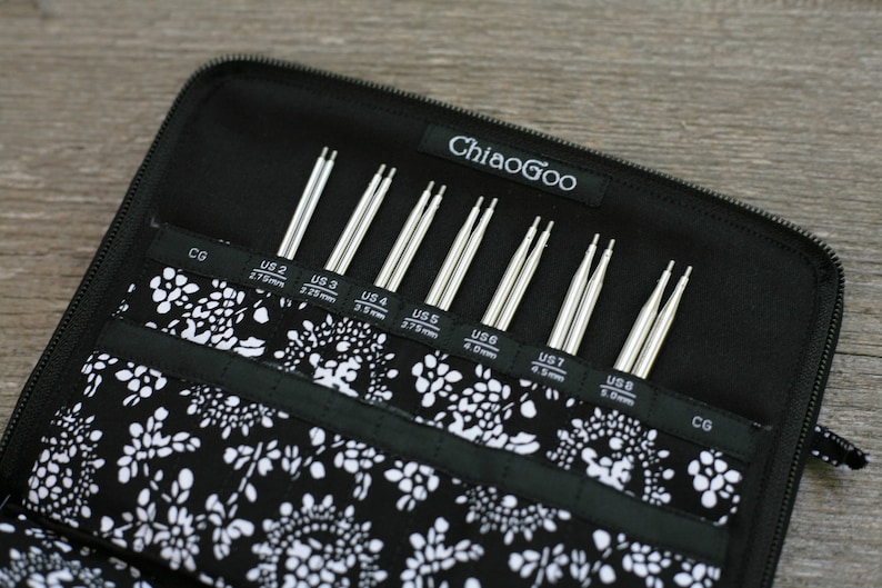 May include: A black zippered case with a white floral pattern holds a set of eight pairs of ChiaoGoo interchangeable knitting needles. The needles are labeled with US sizes 2 through 8, with corresponding millimeter measurements.