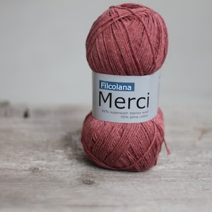 May include: A ball of Filcolana Merci yarn in a reddish-brown color. The label reads "Filcolana Merci 50% superwash merino wool 50% pima cotton".