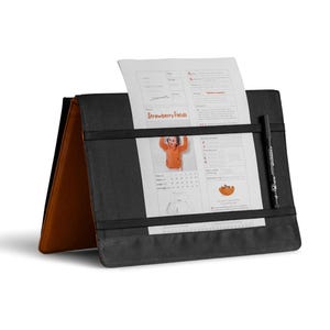 May include: Black document holder with a pen and a sheet of paper that reads "Strawberry Fields". The document holder is open, revealing a brown interior. A black elastic band holds the paper in place.