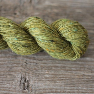 May include: A skein of green yarn with flecks of blue and yellow. The yarn is twisted and has a rough texture.