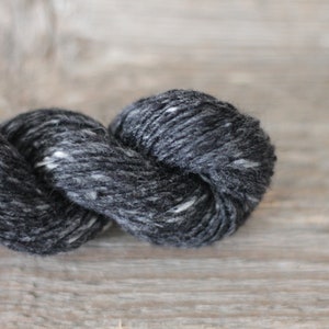 May include: A skein of black yarn with white flecks. The yarn is twisted and looped, showing its texture.