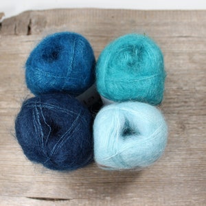 Puede incluir: Cuatro ovillos de lana en tonos azules y verde azulado. La lana es suave y esponjosa, perfecta para tejer o hacer ganchillo.