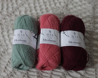 Puede incluir: Tres ovillos de lana en diferentes colores: verde, rosa y burdeos. Cada ovillo tiene una etiqueta que dice "ALVA 100% alpaca 175m/25g filcolana".