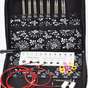 May include: A black zippered case with a white floral pattern lining. The case is open and contains a set of interchangeable knitting needles, a ruler, a red cord, and a variety of colored plastic rings. The case is labeled "ChiaoGoo" and the ruler is labeled "Premium Knitting & Crochet Tools".
