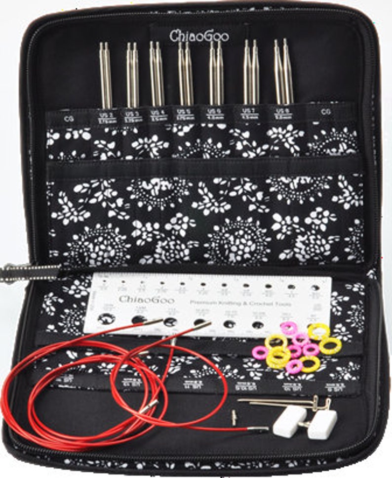May include: A black zippered case with a white floral pattern lining. The case is open and contains a set of interchangeable knitting needles, a ruler, a red cord, and a variety of colored plastic rings. The case is labeled "ChiaoGoo" and the ruler is labeled "Premium Knitting & Crochet Tools".