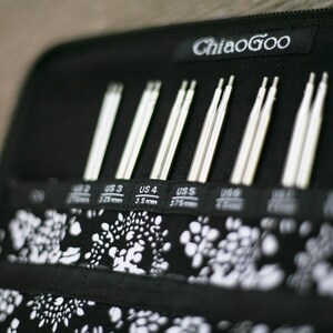 May include: A black zippered case with the text "ChiaoGoo" on the front. The case contains a set of silver knitting needles labeled with US sizes 2, 3, 4, 5, 6, 7, 8, 9, 10, and 11.
