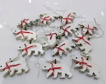 May include: A collection of white polar bear earrings with red ribbon accents. The earrings are made of paper mache and have silver hooks.