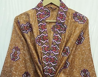 May include: A brown kimono-style robe with a repeating geometric pattern in purple, red, and white. The robe has wide sleeves and a matching tie belt. The robe is hanging on a wooden hanger.