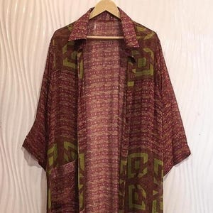 May include: A long, open-front kimono-style robe featuring a deep burgundy base color with a repeating pattern of olive green geometric shapes and thin horizontal lines. The garment has wide, elbow-length sleeves, a classic collar, and two front pockets.