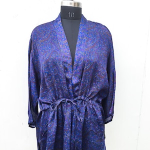Peut inclure: Une veste style kimono bleu foncé ornée d'un motif cachemire complexe aux nuances de violet, rouge et doré. Le vêtement présente des manches trois-quarts, une encolure en V et un lien en tissu fin à la taille pour la fermeture.