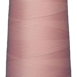 May include: A large, cylindrical spool of dusty rose colored sewing thread. The thread is tightly wound around the central core in a crisscross pattern, creating a textured surface. A white plastic cap is visible at the top of the spool.