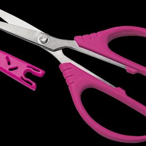 May include: A pair of scissors with a bright pink handle and silver blades, along with a matching pink blade cover. The scissors are designed for precision cutting and are set against a black background.