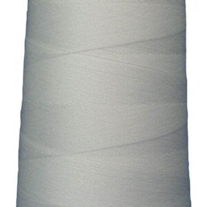 May include: A large, conical spool of light gray sewing thread. The thread is wound tightly around the central core, creating a smooth, uniform texture across the entire surface. A white plastic cap is visible at the top of the spool.