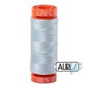 May include: A spool of light gray sewing thread with bright orange plastic ends. The top end features the embossed text AURIFIL, while the bottom end displays the text 100% COTTON. A small white logo with the text AURIFIL is visible on the side.