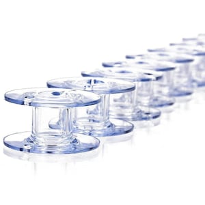May include: A row of clear plastic sewing machine bobbins arranged in a diagonal line. Each bobbin features a cylindrical center core with two flat circular discs at the top and bottom, and a small circular hole near the edge of each disc.
