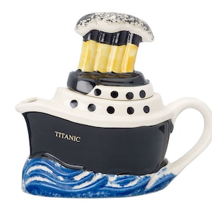 May include: A white and black ceramic teapot shaped like the Titanic with a blue wave base. The teapot has a removable lid with black polka dots and a yellow and black chimney stack.