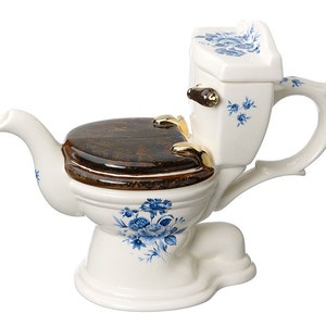 Può includere: Una teiera in ceramica bianca a forma di toilette con un coperchio marrone e un motivo floreale blu.