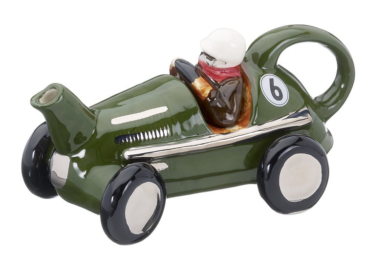 May include: Green ceramic teapot shaped like a vintage race car with a driver figurine inside. The car has a silver trim and black wheels. The teapot has a spout on the front and a handle on the back. The car has the number "6" on the side.
