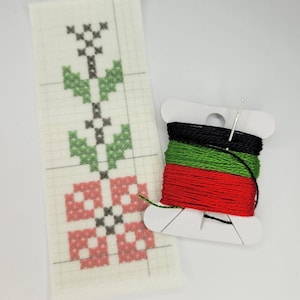 May include: A cross-stitch kit featuring white Aida cloth, a needle, and three spools of embroidery floss in red, green, and black.