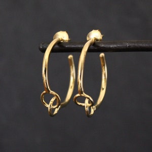 May include: A pair of gold hoop earrings with a knotted detail hanging from each hoop.