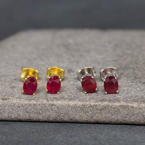 Könnte beinhalten: Vier Paar Rubinohrringe, zwei Paar mit goldenen Fassungen und zwei Paar mit silbernen Fassungen. Die Ohrringe werden auf einer grauen Steinoberfläche präsentiert.