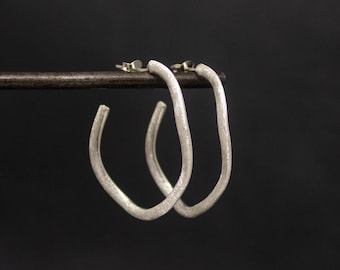 May include: A pair of silver hoop earrings with a slightly irregular, organic shape.