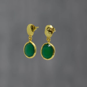 May include: A pair of gold dangle earrings with green oval-shaped gemstones. The earrings have a hammered gold finish.