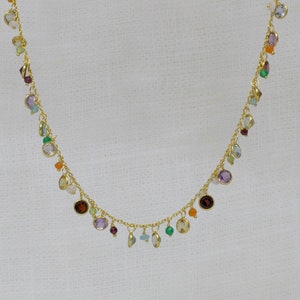 May include: A gold chain necklace with a variety of colorful gemstones hanging from it. The gemstones are in different shapes and sizes, and they include amethyst, aquamarine, citrine, garnet, peridot, and rose quartz.