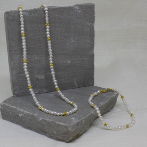 May include: A white pearl necklace and bracelet set with gold accents. The necklace is longer than the bracelet.