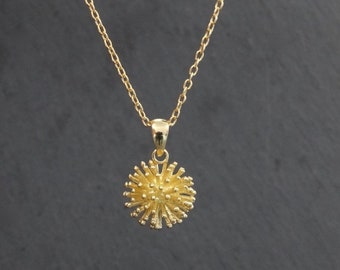 May include: A gold chain necklace with a small, round pendant that resembles a stylized flower or starburst.