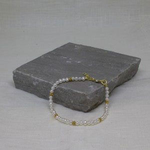 May include: A delicate pearl bracelet with gold accents. The bracelet is made of small white pearls and gold beads, and it has a simple clasp.